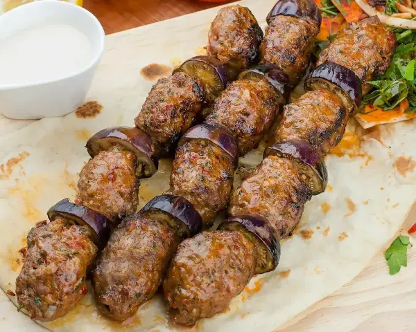Kofta kebab z bakłażanem na płaskim chlebie, podany z sosem.