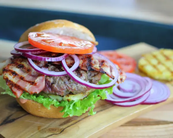 Soczysty burger z chrupiącym boczkiem, pomidorem, sałatą i czerwoną cebulą. Dodatki do burgera kuszą smakiem.