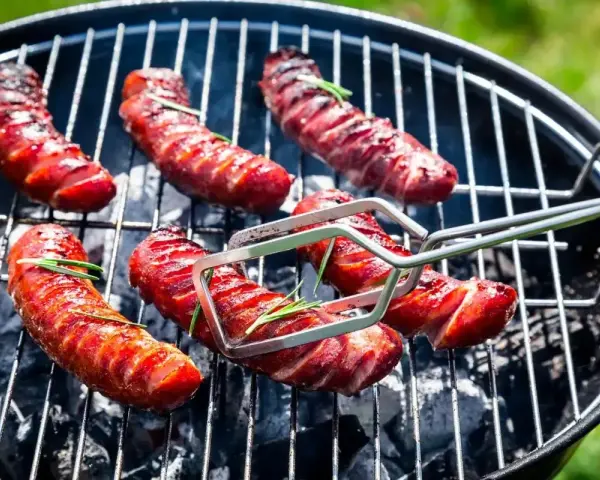 Aromatyczna kiełbasa z grilla, skwiercząca na węglu, z gałązkami rozmarynu. Idealna na letnie popołudnie.