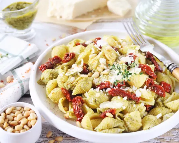 Pyszny makaron z pesto i suszonymi pomidorami, posypany parmezanem i orzeszkami pinii.