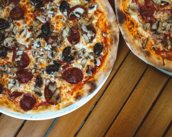 Dwie pizze z bogactwem składników na wierzchu: salami, pieczarki i czarne oliwki. Idealne na wspólny posiłek.