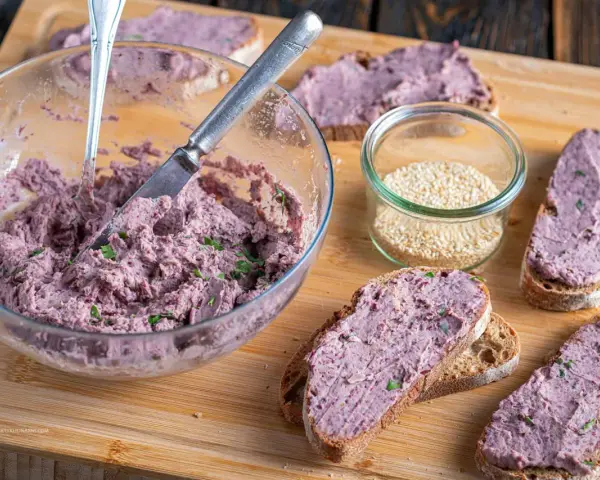 Pyszna pasta z czerwonej fasoli na chlebie, obok słoiczek sezamu. Idealna na szybką przekąskę.
