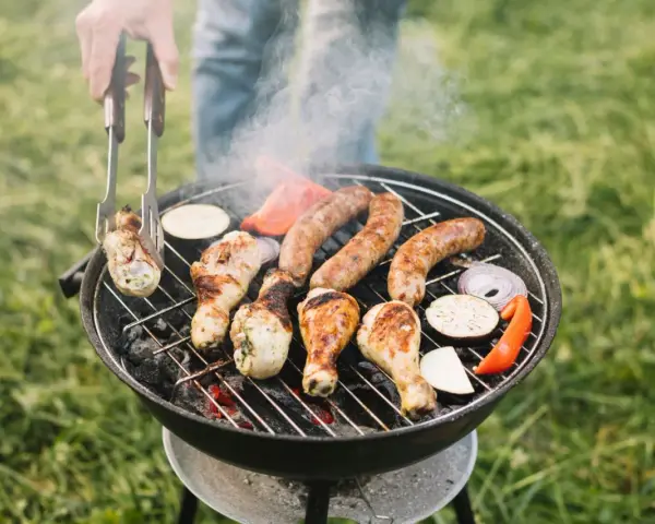 Pyszne kiełbaski i kurczak pieką się na grillu, a dym unosi się w powietrzu. Idealny sposób, jak rozpalić grilla i cieszyć się latem.
