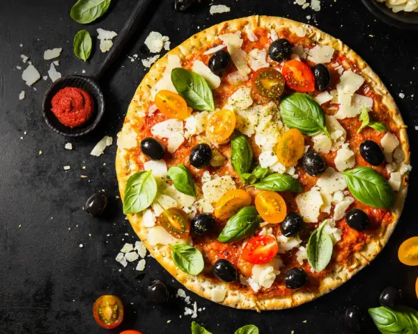 Pizza z pomidorkami, oliwkami i bazylią. Pomidorowe pesto to niezbędny dodatek smakowy włoskiej pizzy.