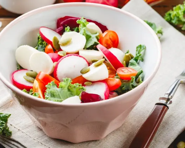 Świeża sałatka do grilla w 3 minuty: rzodkiewka, pomidorki, ser mozzarella i pestki dyni w misce.