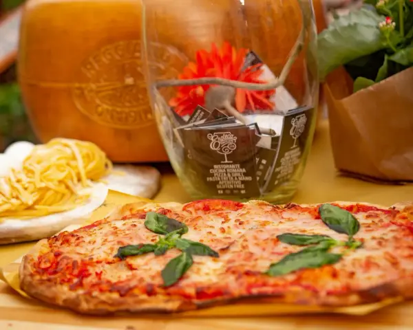 Pyszne rodzaje pizzy, makaron i ser parmezan. W tle szklany wazon z ozdobami i kwiatami.