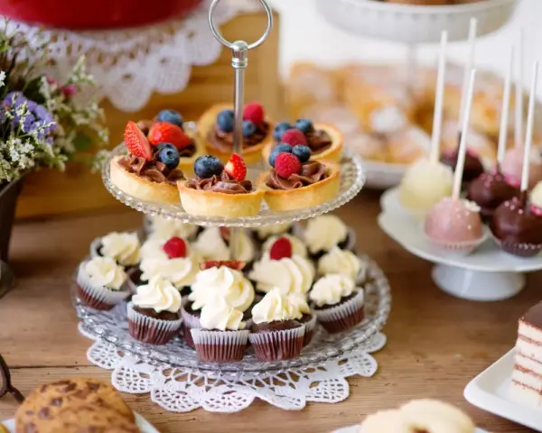 Słodkie przekąski: babeczki, tartaletki z owocami, cake pops i ciasto czekoladowe na drewnianym stole.