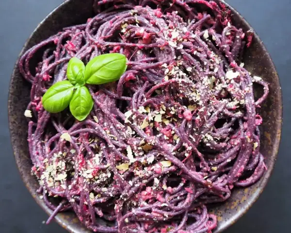 Fioletowy makaron z buraczanym pesto ze słoika, posypany orzechami i udekorowany listkiem bazylii.