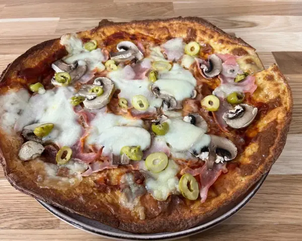 Apetyczna pizza z twarogu z pieczarkami, szynką i oliwkami, z ciągnącym się serem.
