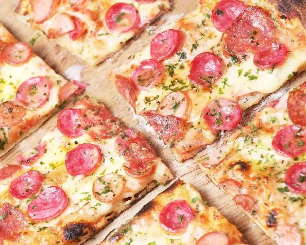 Kawałki pysznej pizzy cienkie ciasto z kiełbasą i serem, posypane ziołami. Idealna na szybką przekąskę.