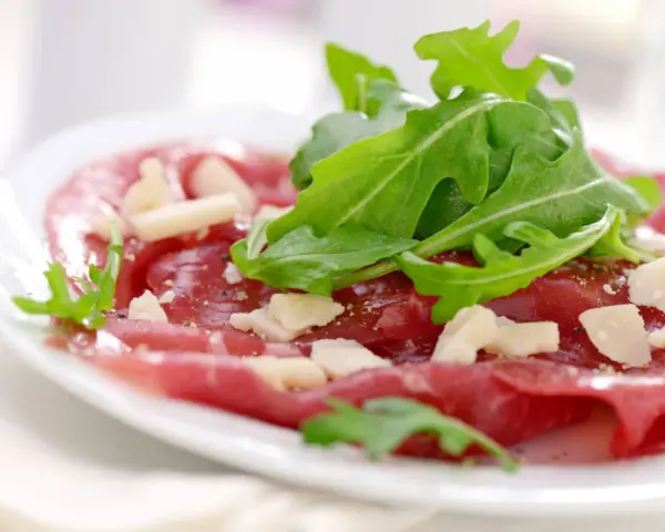 Cienkie plastry wołowiny z rukolą i parmezanem, polane pysznym sosem do carpaccio.