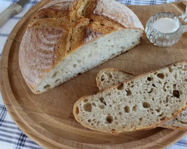 Chleb pszenno żytni na zakwasie, pokrojony na desce, z solniczką i nożem w tle.