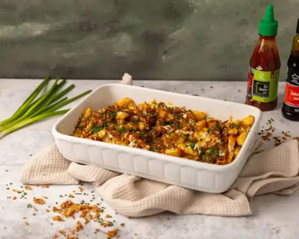 Pyszne frytki z chrupiącą posypką i sosem. Obok butelki sosu Sriracha i Tonkatsu, idealne do frytek.