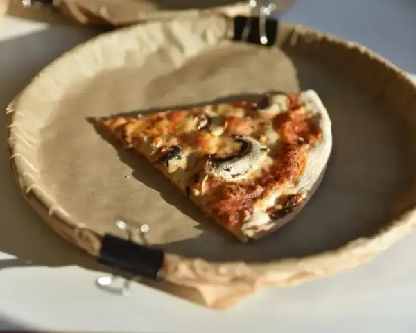 Kawałek pizzy z pieczarkami na brązowym papierze. Zastanawiasz się, ile kalorii ma pizza?