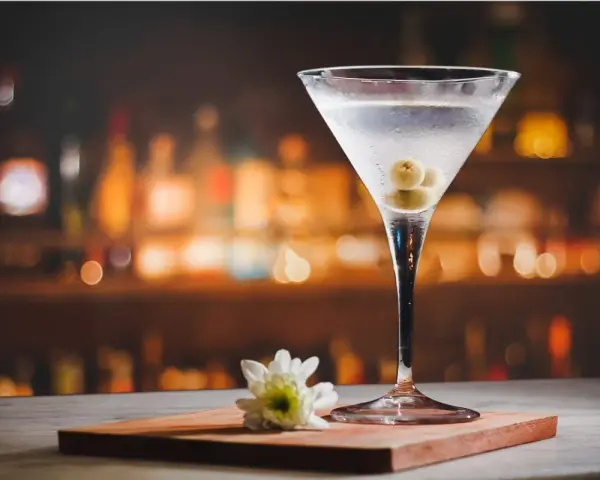 Kryształowy kieliszek z martini, trzema oliwkami i białą kwiatową ozdobą. Idealny drink, z czym pić martini?