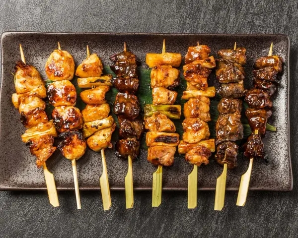 Różnorodne yakitori na talerzu: kurczak, warzywa i inne przysmaki, apetycznie wyglądające i gotowe do jedzenia.