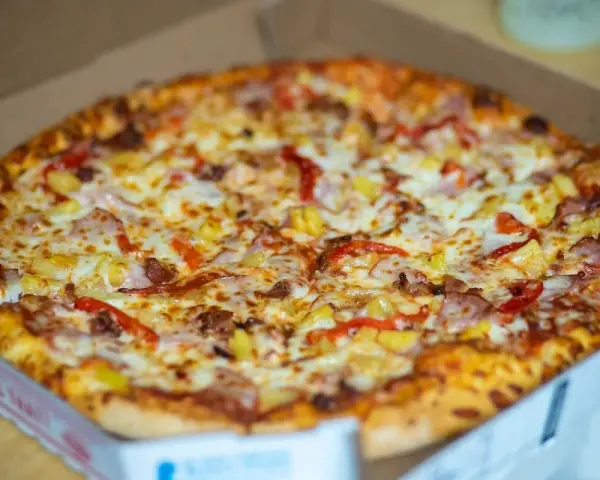 Pyszna, gorąca mrożona pizza w mikrofali, prosto z pudełka. Złocisty ser, kawałki ananasa i papryki kuszą apetycznie.