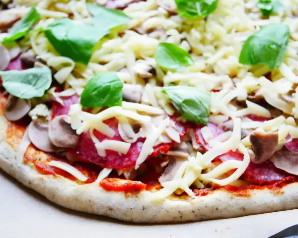 Gotowy do pieczenia przepis na ciasto do pizzy: sos pomidorowy, salami, pieczarki, ser i świeża bazylia.