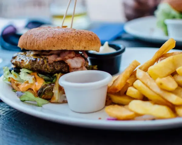 Pyszny burger z bekonem i frytki na talerzu. Idealny sposób, jak jeść burgera w restauracji, by delektować się każdym kęsem.