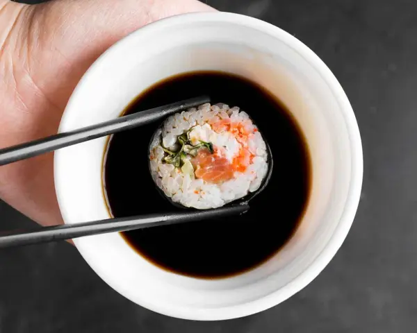 Pałeczki trzymają sushi z łososiem, zanurzając je w ciemnym sosie do sushi.