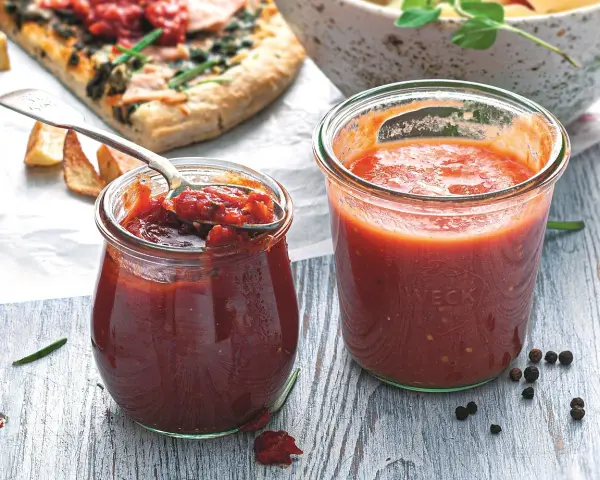 Dwa słoiczki Weck z domowymi dipami pomidorowymi, obok kawałek pizzy i miska makaronu. Idealne do pizzy i nie tylko!