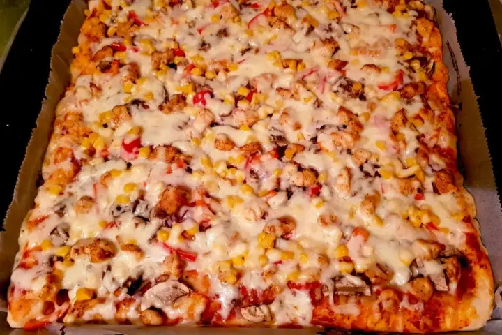 Pyszny przepis na pizzę z kurczakiem, kukurydzą i pieczarkami, obficie posypaną ciągnącym się serem.