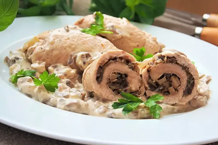 Roladki z indyka duszone w sosie grzybowym, podane na białym talerzu z natką pietruszki.
