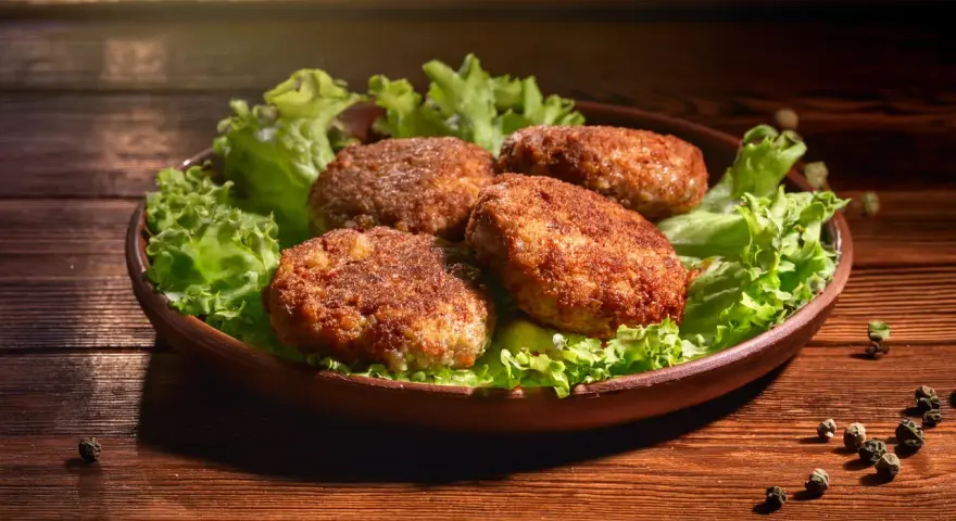 Cztery apetyczne kotlety mielone z airfryer, podane na liściach sałaty. Idealne na szybki obiad.