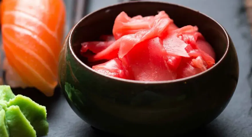 Miseczka z różowym, marynowanym imbirem obok sushi i wasabi. Idealny dodatek do japońskich potraw.