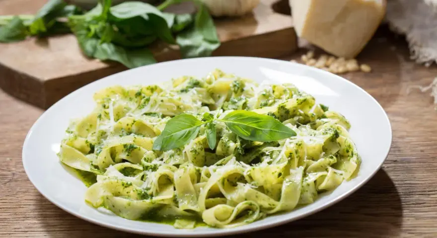 Talerz tagliatelle z aromatycznym pesto z rukoli, posypany parmezanem i udekorowany listkami bazylii.