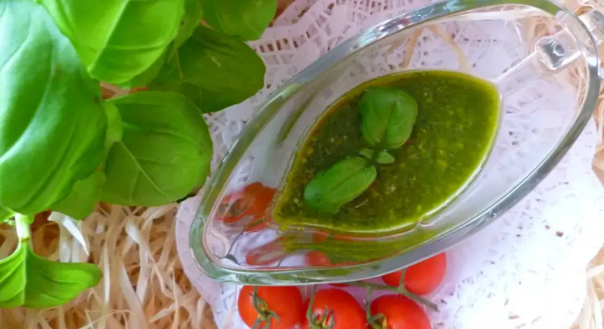 Świeże liście bazylii i pomidorki koktajlowe obok sosu pesto z bazylii w szklanym naczyniu.