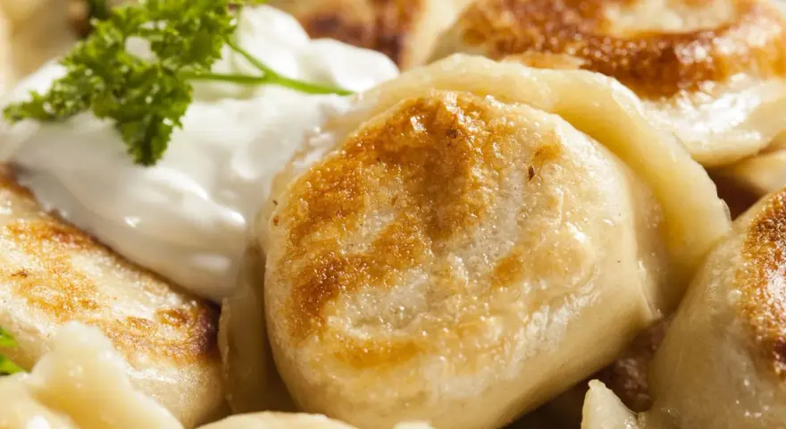 Złociste, usmażone pierogi z serem, podane ze śmietaną i natką pietruszki. Idealne na obiad, gdy szukasz przepisu na miękkie ciasto na pierogi.