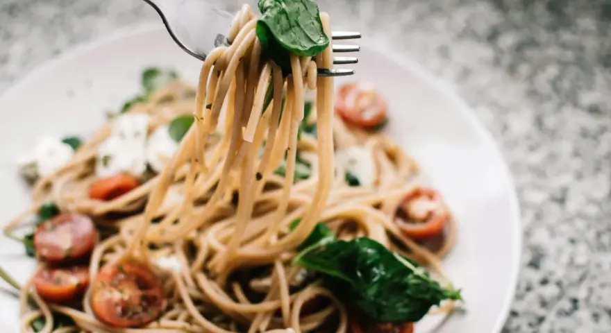 Widelec podnosi porcję spaghetti z pomidorkami i mozzarellą. Czy makaron to węglowodany? Tak, to pyszne źródło energii!