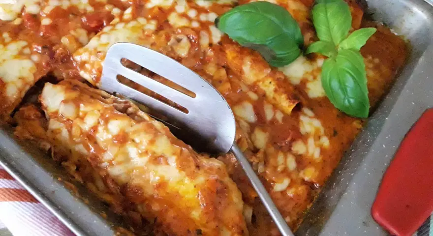 Zapiekana tortilla z mięsem mielonym, polana sosem pomidorowym i posypana serem, ozdobiona listkami bazylii.
