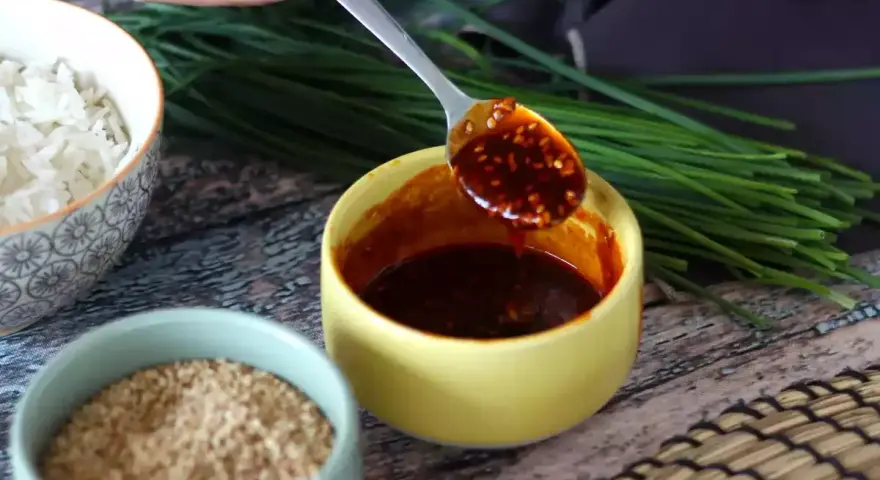 Łyżka z aromatycznym sosem gochujang, obok miseczki ryżu, sezamu i szczypiorku.