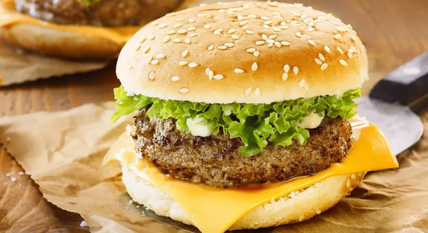 Zbliżenie na cheeseburgera z serem, sałatą i majonezem na bułce z sezamem.