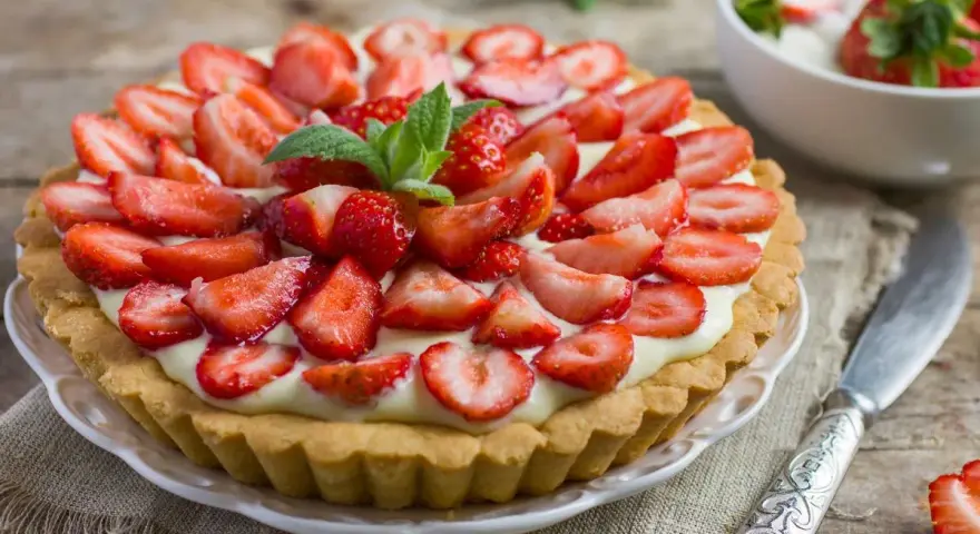 Tarta z truskawkami i kremem, ozdobiona listkami mięty.