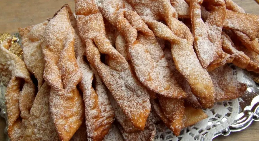 Chrupiące faworki, przepis babci, posypane cukrem pudrem, ułożone na ozdobnej tacy.