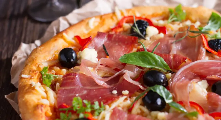 Pyszna pizza z cienko pokrojoną, aromatyczną szynką, czarnymi oliwkami i papryką. Idealna jaka szynka na pizzę!