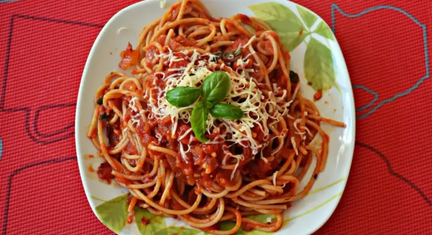 Pyszny sos do makaronu spaghetti z tartym serem i bazylią na talerzu.