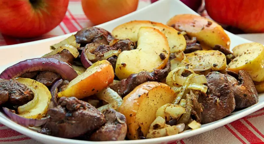 Pyszna wątróbka z jabłkiem, cebulą i grzybami na białym talerzu. Aromatyczne danie gotowe do podania.
