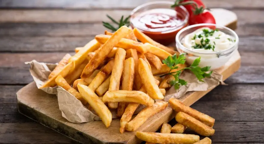 Złociste frytki na desce, idealne co do frytek na szybko. Obok ketchup i majonez.