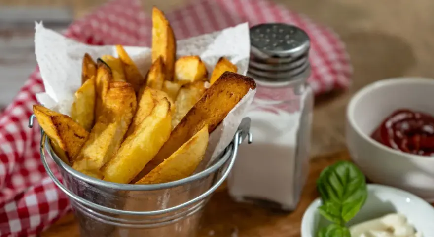 Złociste frytki w metalowym wiaderku, obok solniczka i ketchup. Czy ziemniaki sałatkowe nadają się na frytki? Wyglądają pysznie!