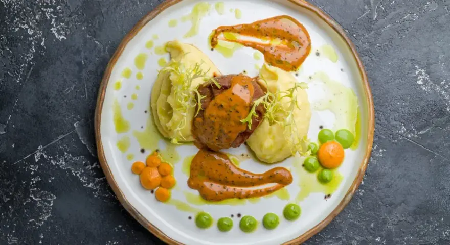 Mięso z puree ziemniaczanym, ozdobione pomarańczowym sosem do mielonych i zielonymi groszkami.