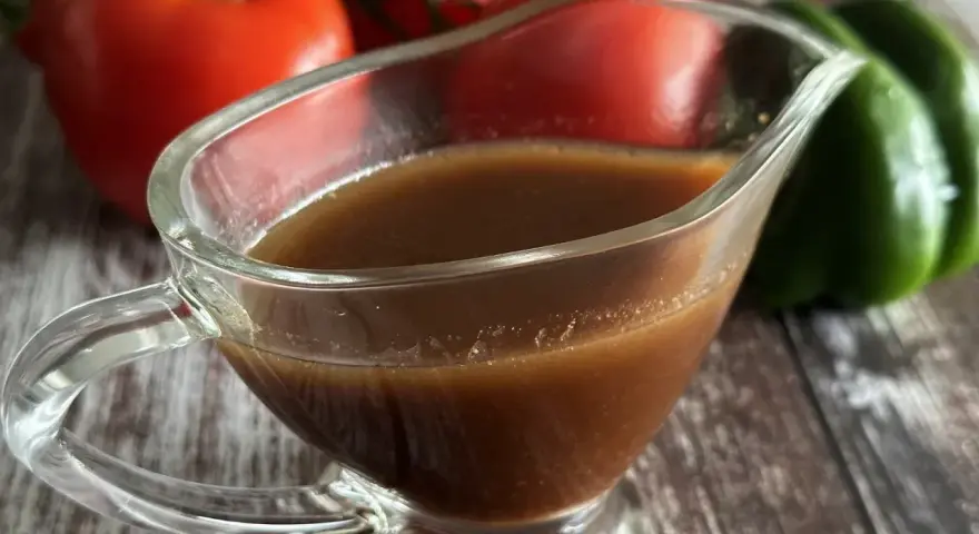Sos balsamiczny w sosjerce, w tle pomidory i zielona papryka. Idealny do sałatek i mięs.