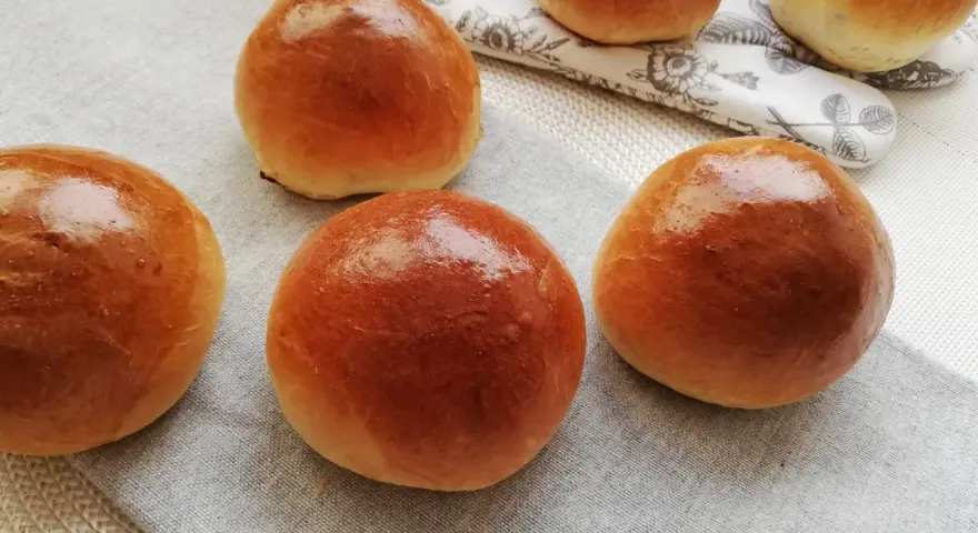 Pięć puszystych bułek maślanych, lśniących od pieczenia, ułożonych na lnianej serwetce.