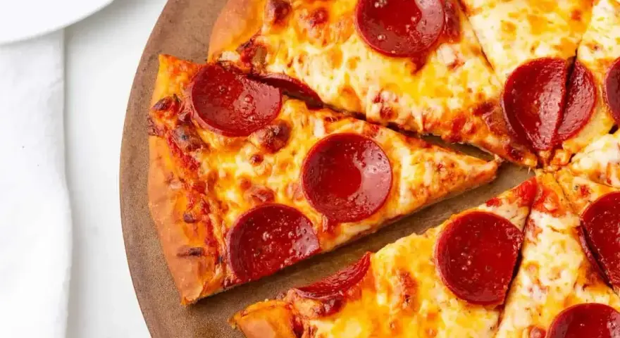 Kawałki pizzy z serem i okrągłymi plasterkami peperoni, ułożone na drewnianej desce.