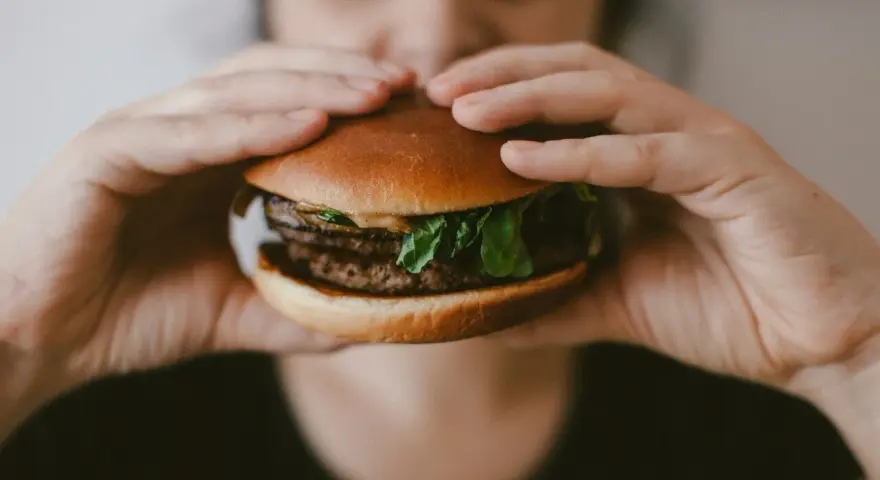 Osoba trzyma soczystego burgera, zastanawiając się, ile kalorii ma burger w restauracji.