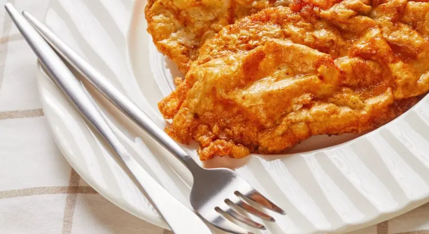 Złocisty kotlet słoneczny na białym talerzu, obok sztućce. Idealny na słoneczny dzień.