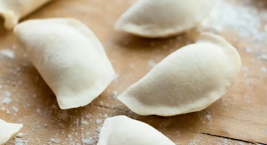 Surowe pierogi uformowane na drewnianej desce. To ciasto na pierogi bez jajka, gotowe do nadzienia.